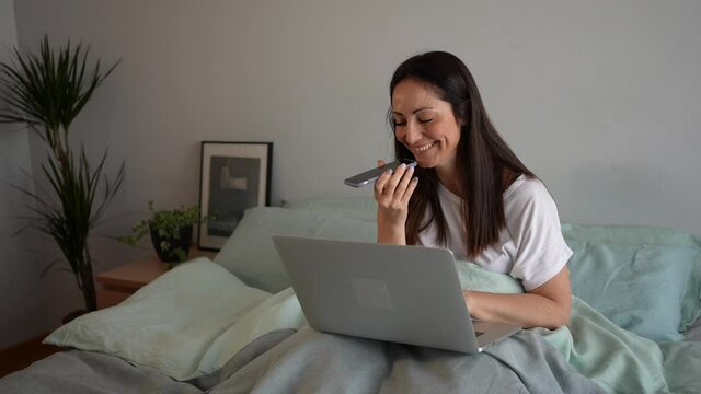 A happy woman using speakerphone for conversation with her friend while working from home. Businesswoman using audio application to send voice message.