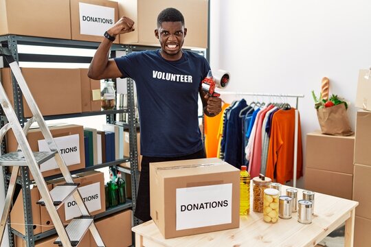 Young african american volunteer man packing donations box for charity strong person showing arm muscle, confident and proud of power
