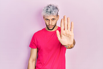 Young hispanic man with modern dyed hair wearing casual pink t shirt doing stop sing with palm of...