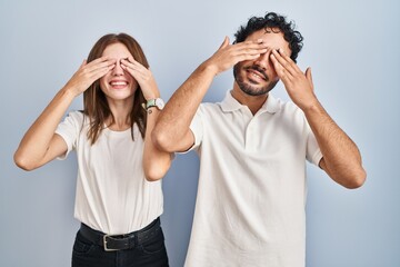 Young couple wearing casual clothes standing together covering eyes with hands smiling cheerful and funny. blind concept.