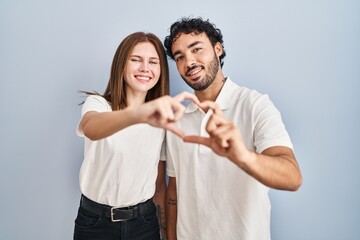 Young couple wearing casual clothes standing together smiling in love doing heart symbol shape with hands. romantic concept.