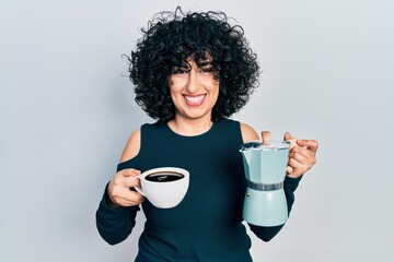 Young middle east woman holding italian coffee maker winking looking at the camera with sexy...