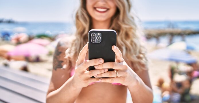 Young blonde girl using smartphone sitting on the bench at the beach.