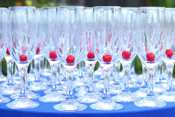 A row of champagne glasses with red  cherries on a blue table. Drink relax concept. Glasses on a table bar. Empty wine glasses with cherries served in a restaurant. Celebration. Champagne glasses