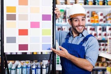 Happy professional painter showing stand with samples in paint shop