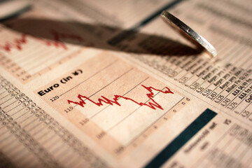 Stock Market Graph next to a falling Eurocoin. Red trend line indicates the stock market recession...