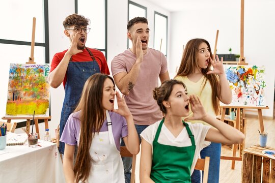 Group of five hispanic artists at art studio shouting and screaming loud to side with hand on mouth. communication concept.