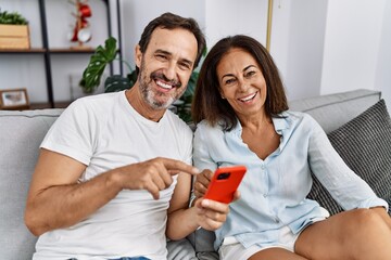 Middle age man and woman couple using smartphone sitting on sofa at home