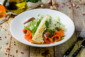 Caesar salad with salmon on wooden table