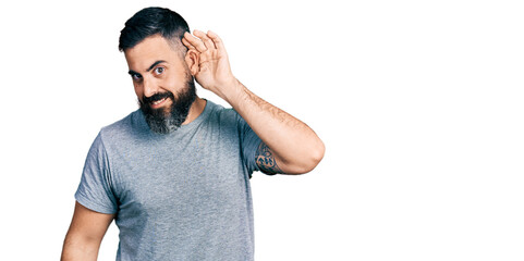Fototapeta premium Hispanic man with beard wearing casual grey t shirt smiling with hand over ear listening and hearing to rumor or gossip. deafness concept.