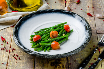 Fried green beans with sauce and tomatoes on wooden table