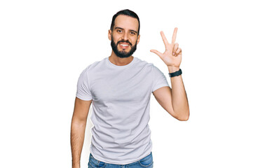 Fototapeta premium Young man with beard wearing casual white t shirt showing and pointing up with fingers number three while smiling confident and happy.