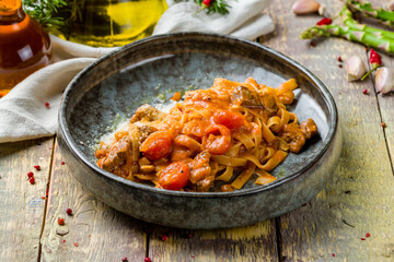 Pasta fettuccine with beef and tomatoes on wooden table
