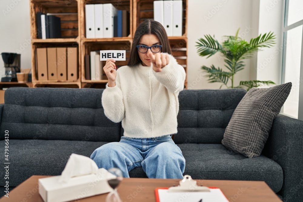 Poster Young hispanic woman going to therapy at consultation office asking for help pointing with finger to the camera and to you, confident gesture looking serious