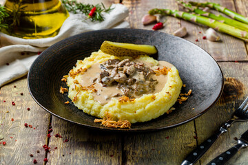 Stroganoff with mashed potatoes on black plate on wooden table