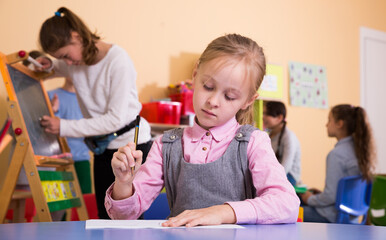 Little schoolgirl drawing in break between lessons in elementary school