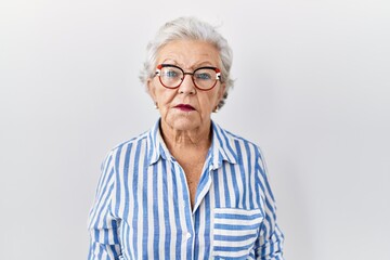 Senior woman with grey hair standing over white background relaxed with serious expression on face. simple and natural looking at the camera.