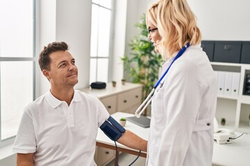 Obraz premium Middle age man and woman doctor and patient using tensiometer having medical consultation at clinic