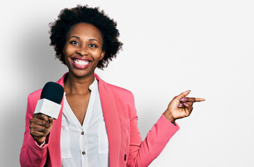 African american woman with afro hair holding reporter microphone smiling happy pointing with hand and finger to the side
