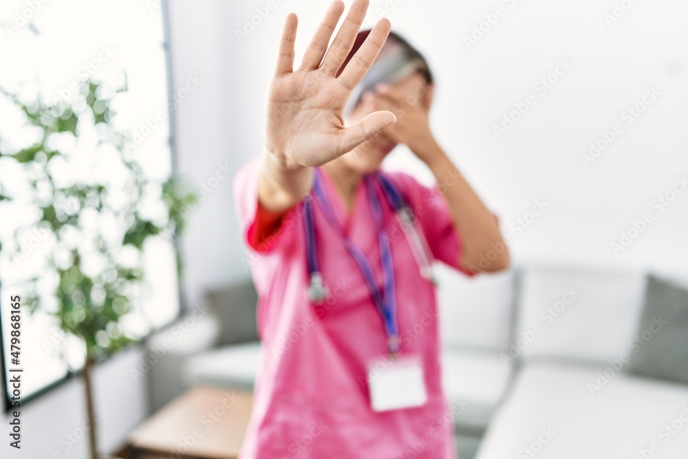 Sticker young beautiful woman wearing doctor uniform and stethoscope covering eyes with hands and doing stop