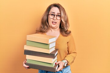Middle age caucasian woman holding a pile of books clueless and confused expression. doubt concept.
