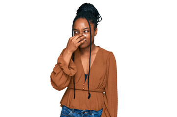 Young african american woman wearing casual clothes smelling something stinky and disgusting, intolerable smell, holding breath with fingers on nose. bad smell