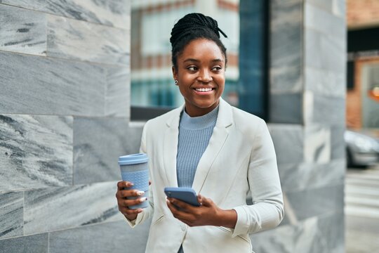 Young african american businesswoman using smartphone and drinking coffee at the city.