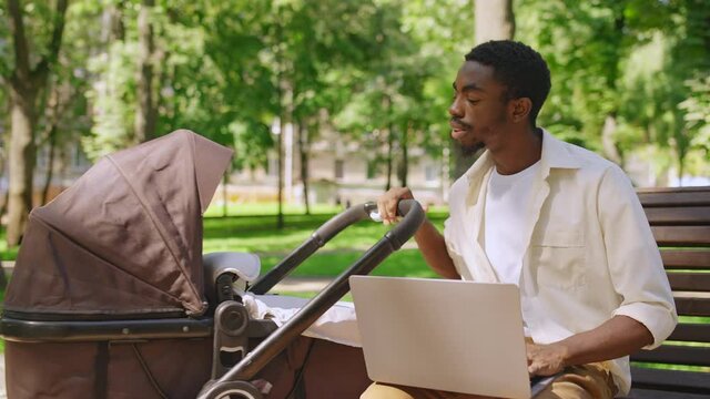 Young father freelancer working on laptop and rocking baby stroller in park