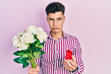 Young hispanic man holding bouquet of flowers and wedding ring depressed and worry for distress, crying angry and afraid. sad expression.