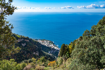 Fototapeta na wymiar The Italian village of Praiano, seen from above, from the Path of the Gods (Sentiero degli Dei) along the scenic Amalfi Coast of Italy, with the blue Tyrrhenian Sea and blue sky and clouds