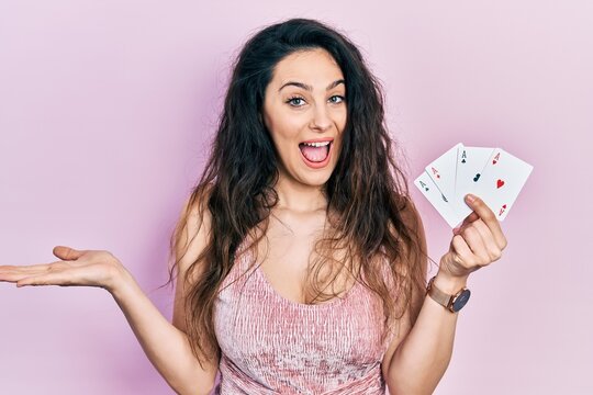 Young hispanic woman holding poker cards celebrating achievement with happy smile and winner expression with raised hand