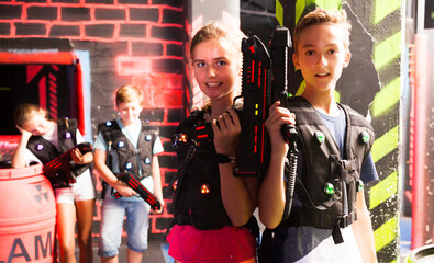 Fototapeta na wymiar Portrait of excited teen boy and girl with laser guns during lasertag game in dark room..