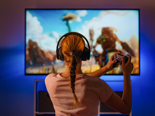 Shooter girl plays a video game. She has a joystick in her hands, headphones on her head. There is...