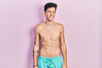 Fototapeta premium Young hispanic man wearing swimwear shirtless looking away to side with smile on face, natural expression. laughing confident.