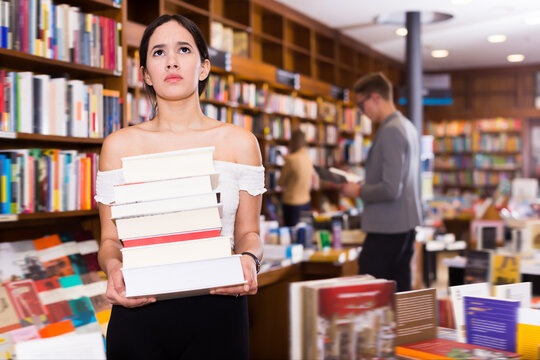 Smiling female student standing in library with pile of books in hands