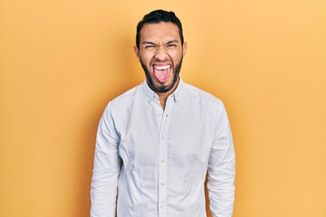 Hispanic man with beard wearing business shirt sticking tongue out happy with funny expression. emotion concept.