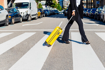 Unrecognizable business woman with a yellow suitcase crossing a crosswalk in the city. Woman on business trip.