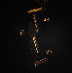Brown cinnamon sticks and star anise with gold dust in motion on a black background. Cooking,...