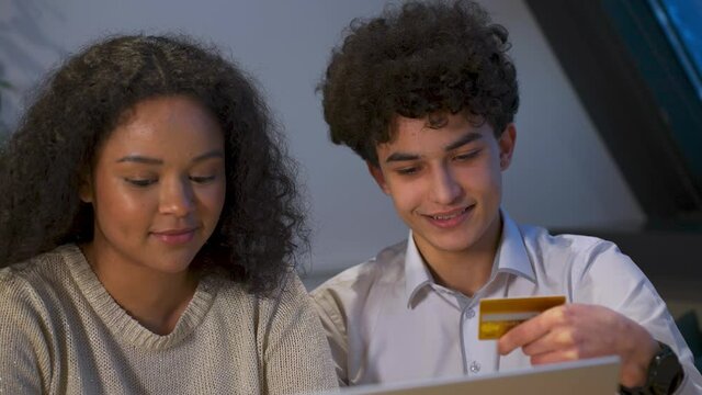 Happy attractive African-American a young couple of zoomers shopping online the guy helps the girl enter the card details into laptop. After the purchase, they hugging rejoice and have fun. 