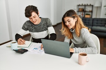 Young couple smiling happy working using laptop sitting on the table at home.