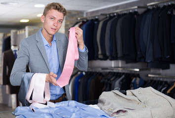 Adult male purchaser in shirt choosing tie in the clothes store