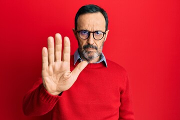 Middle age hispanic man wearing casual clothes and glasses doing stop sing with palm of the hand. warning expression with negative and serious gesture on the face. - obrazy, fototapety, plakaty