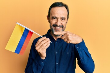 Middle age hispanic man holding colombia flag smiling happy pointing with hand and finger