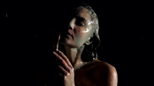 beautiful woman is showering off mud from her face, body and hair after beauty wrap in spa
