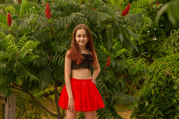 Teenage girl in a black top and red skirt on a summer wood background. Holidays. Girl 10 years old.