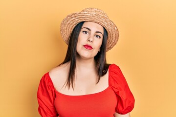 Young hispanic woman wearing summer hat relaxed with serious expression on face. simple and natural looking at the camera.