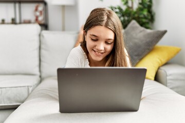 Adorable girl using laptop lying on sofa at home