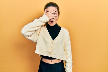 Young brunette girl wearing casual yellow jacket peeking in shock covering face and eyes with hand, looking through fingers afraid