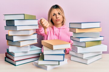 Young caucasian woman sitting on the table with books looking unhappy and angry showing rejection...
