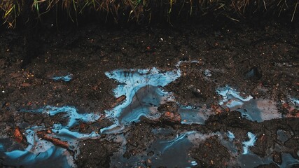 Smudges of Toxic Industrial Liquid Chemical Pollutant Visible on Surface of Rain Water Puddles on...